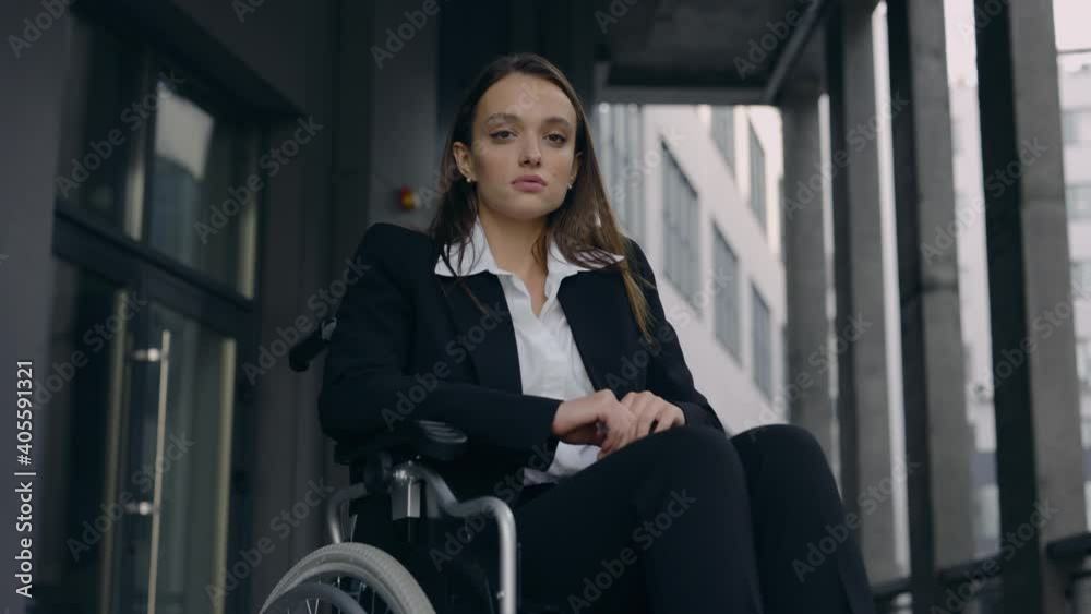 Portrait of handicapped beautiful woman ceo executive in suit sitting in wheelchair at top of office building stairs. Disabled attractive female person looking to camera outdoors. Portrait of handicapped beautiful woman ceo executive in suit sitting in wheelchair at top of office building stairs. Disabled attractive female person looking to camera outdoors.