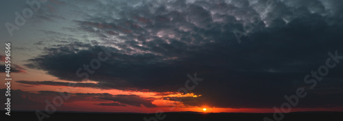 Dramatic gloomy panorama of bright saturated sunset with many dark clouds