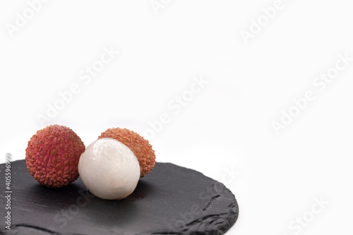 Open and unpeeled lychee fruit on a black slate tray