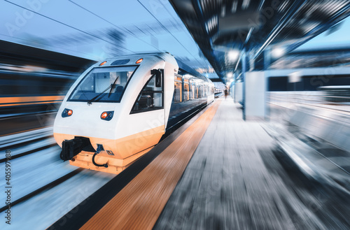 High speed train in motion on the railway station at night. Modern intercity passenger train with motion blur effect on the railway platform. Industrial. Railroad in Europe. Commercial transportation
