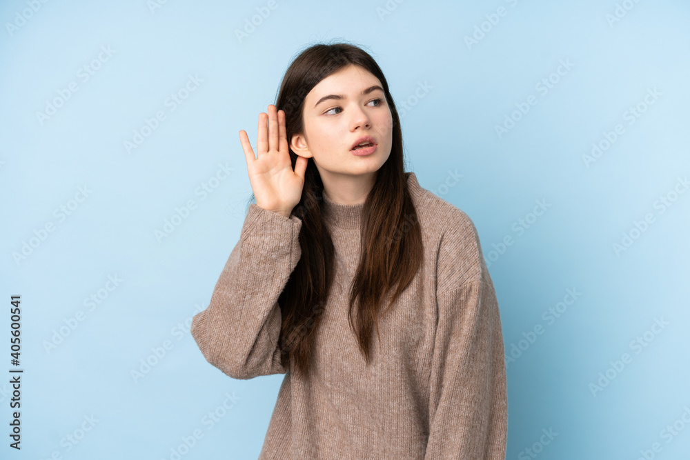 Young Ukrainian teenager girl wearing a sweater over isolated blue background listening to something by putting hand on the ear Young Ukrainian teenager girl wearing a sweater over isolated blue background listening to something by putting hand on the ear