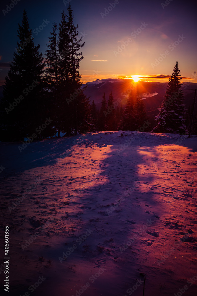 The first rays of the sun rising from behind the mountains illuminate the snowy slopes