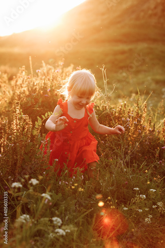 Portrait of a little beautiful girl in red dress on nature on summer day vacation. The playing in the green field at the sunset time. Close Up. The concept of family holiday and time together.