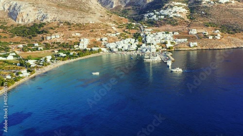 Drone video of Aegialis in Greece. Drone flies high over the small town, that is surrounded by mountains, and clear blue water. There is a small marina, and there is a boat sailing towards the harbour photo