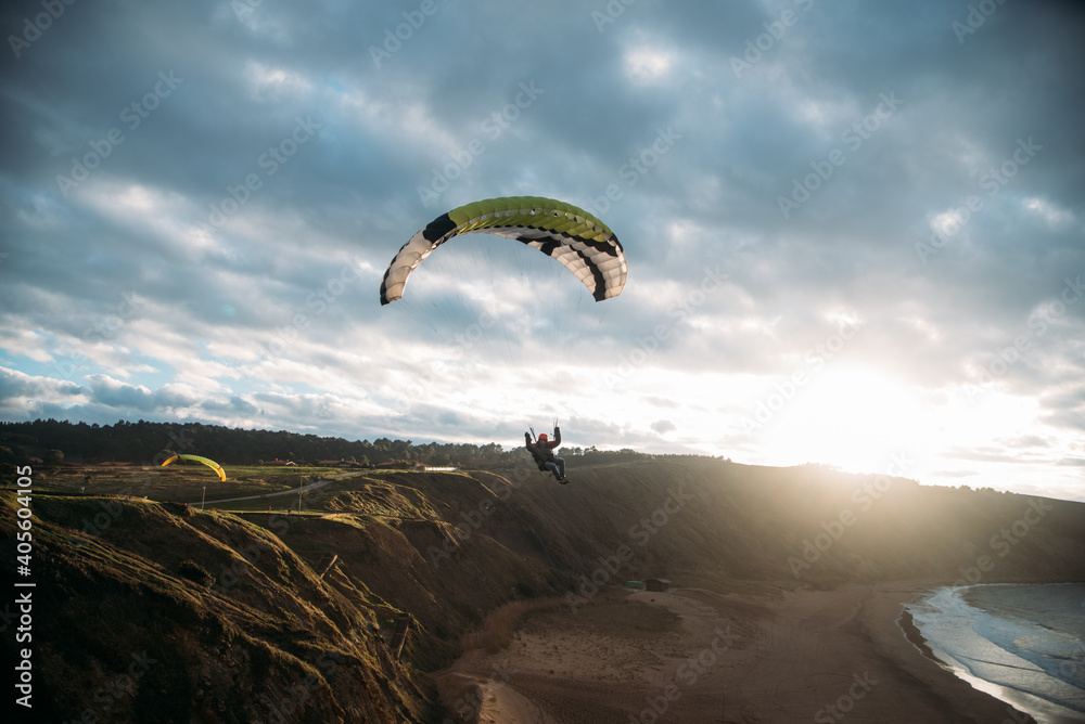 Gente haciendo parapente en un acantilado con la playa debajo y un atardecer Gente haciendo parapente en un acantilado con la playa debajo y un atardecer