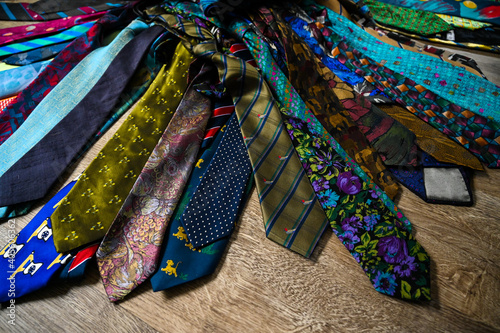 A bundle of colorful, oldfashioned business ties is lieing on a wooden floor.