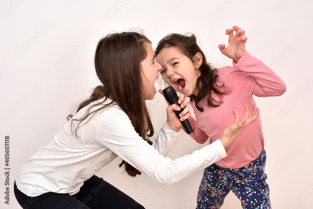 Two happy sisters fooling around and singing a song on a microphone. Emotional portrait of happy children. Two happy sisters fooling around and singing a song on a microphone. Emotional portrait of happy children.