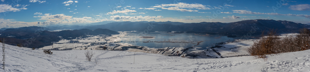 Wide panorama of lake cerknica on a cold winter day, visible lake with water and snow on the fields. Slope of Slivnica mountain in the foreground.
