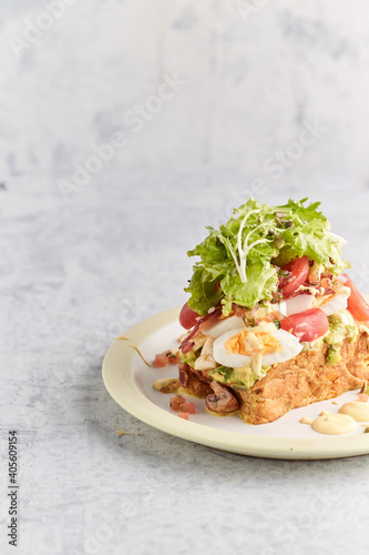 French toast stacked high and topped with salmon, lettuce, cheese, apple, whip cream and maple syrup in a warm, rustic, inviting restaurant atmosphere.
