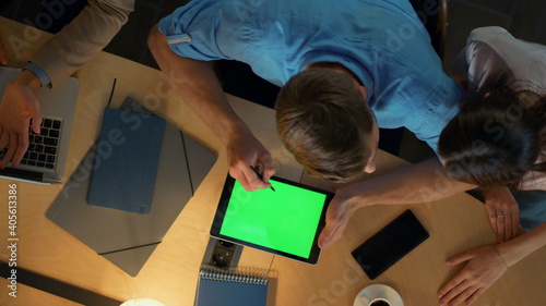 Man using stylus on tablet indoors. Busy team discussing work issues in office.