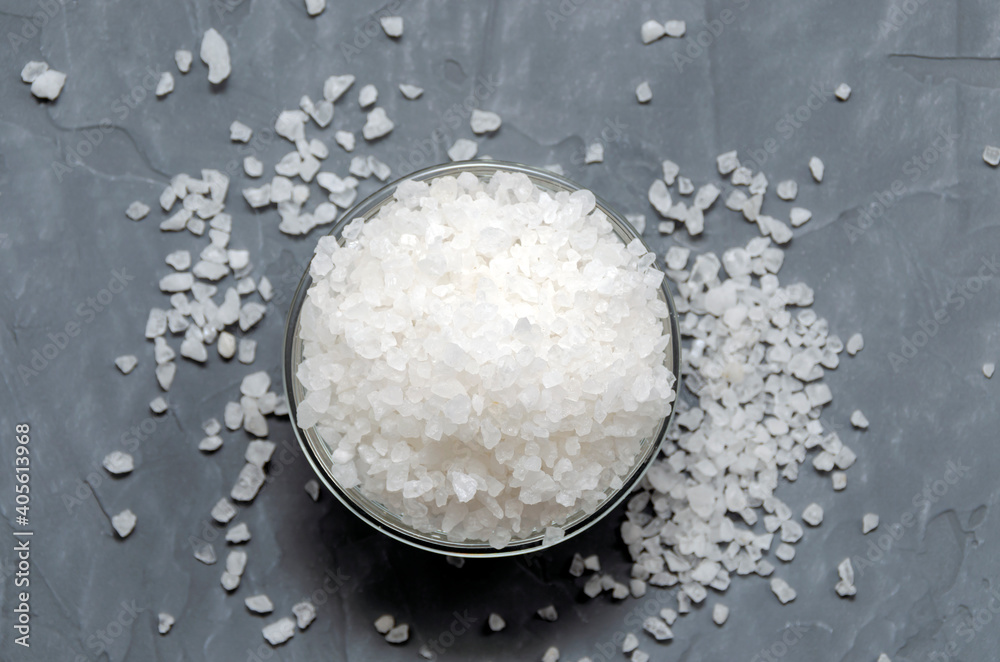 coarse white sea salt in a glass bowl is scattered on the table - top view. On a gray concrete background. coarse white sea salt in a glass bowl is scattered on the table - top view. On a gray concrete background.
