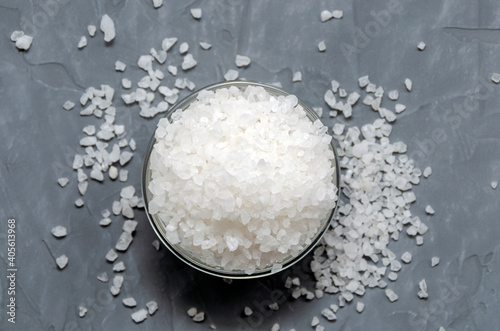 coarse white sea salt in a glass bowl is scattered on the table - top view. On a gray concrete background.