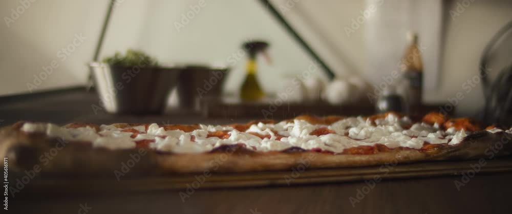 Chef spreading salt over a ready burrata al taglio pizza. Close up, slow motion