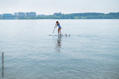 Caucasian woman in a striped swimsuit rides on a SUP board. The girl prefers active rest. © Михаил Решетников