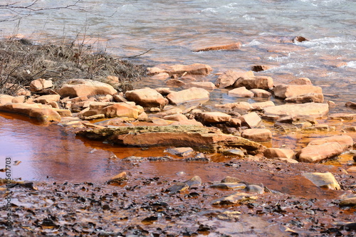 Orange acid abandoned coal mine drainage water entering clean water stream with rocks in Western Pennsylvania
