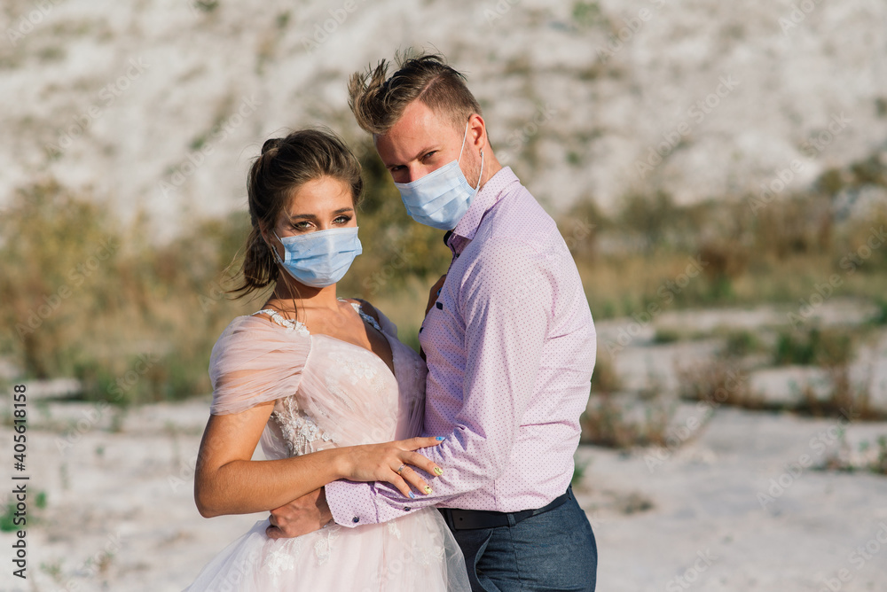 Young loving couple in medical masks in park during quarantine on wedding day. Young loving couple in medical masks in park during quarantine on wedding day.