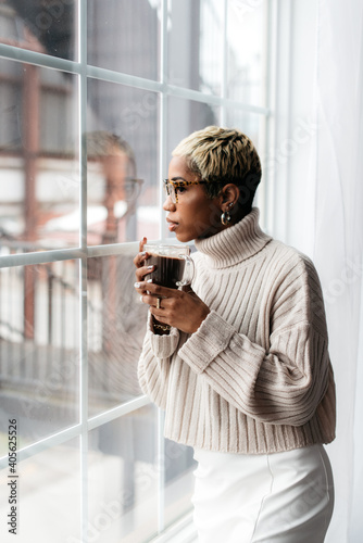 Beautiful black woman holding coffee looking out the window