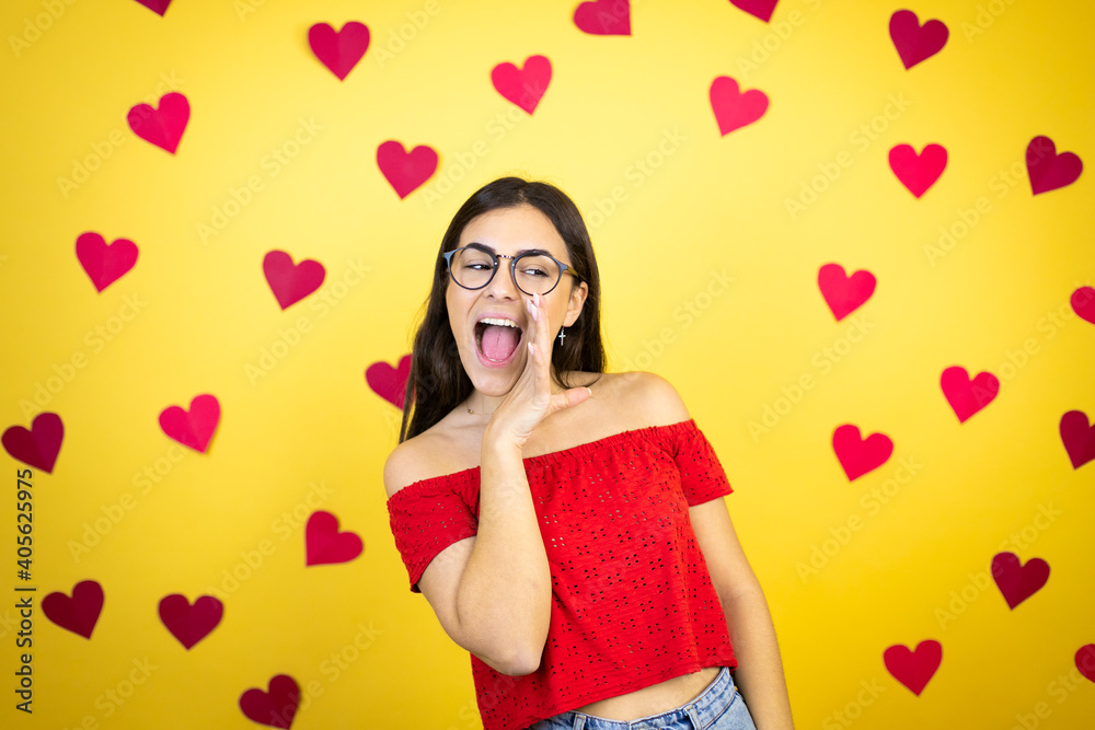 Young beautiful woman over yellow background with red hearts hand on mouth telling secret rumor, whispering malicious talk conversation Young beautiful woman over yellow background with red hearts hand on mouth telling secret rumor, whispering malicious talk conversation