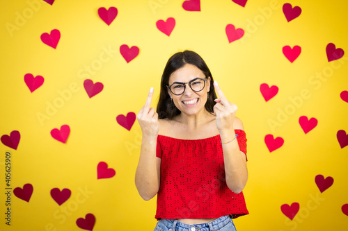 Canvas Print Young beautiful woman over yellow background with red hearts showing middle finger doing fuck you bad expression, provocation and rude attitude