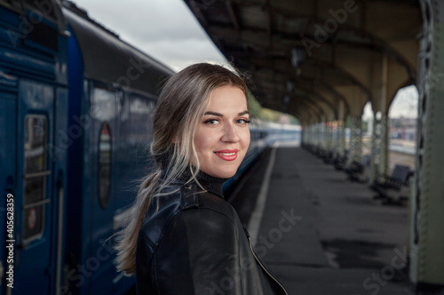 Portrait of a young beautiful woman in a leather jacket on a perone next to the train at the railway station. Waiting for the train Vitebsk station St. Petersburg.