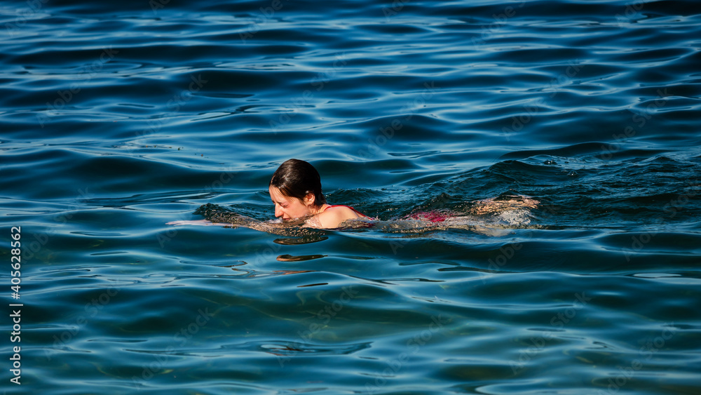 A young girl swims in the crystal clear water of a mountain lake.