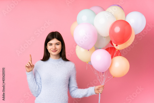 Young Ukrainian teenager girl holding lots of balloons over isolated pink background pointing with the index finger a great idea