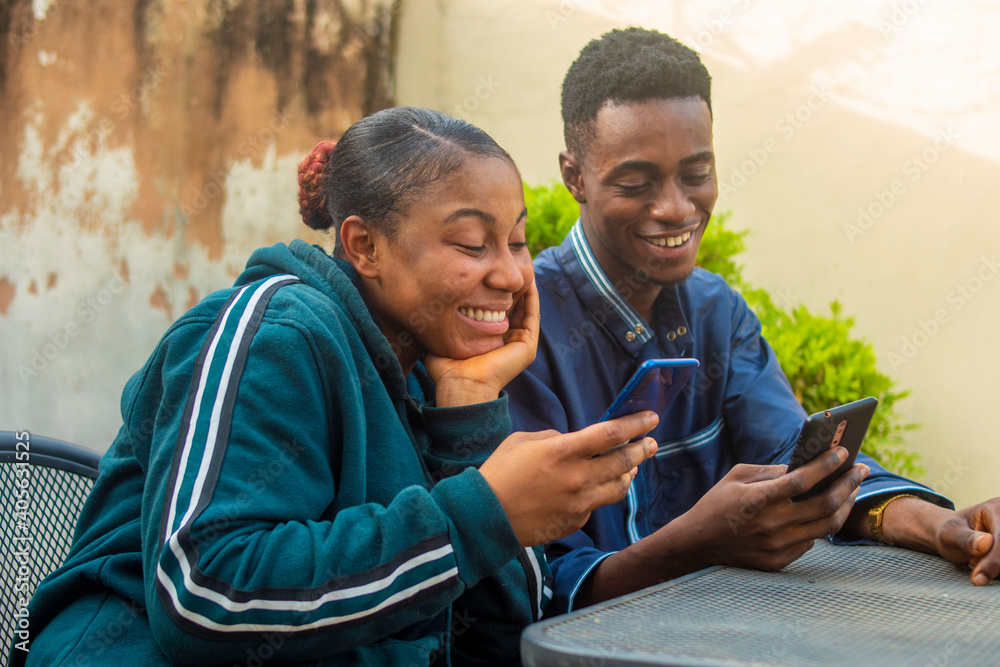 Obraz premium young black man and lady happy together with their smart phones while sitting outdoor.