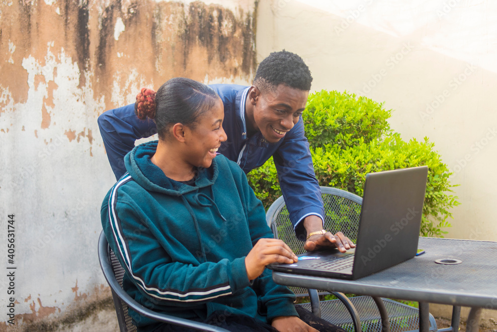 young black man and lady happy together operating a laptop while sitting outdoor.