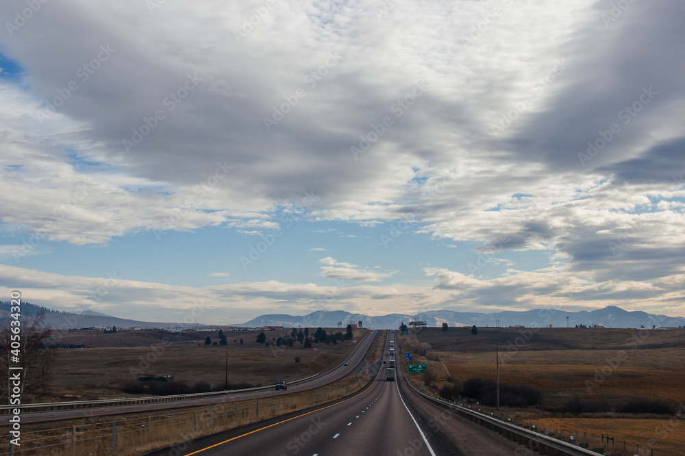 Beautiful autumn landscape on a bright sunny day, which depicts a highway, high mountains ahead and a clear blue sky with fluffy gray-white clouds