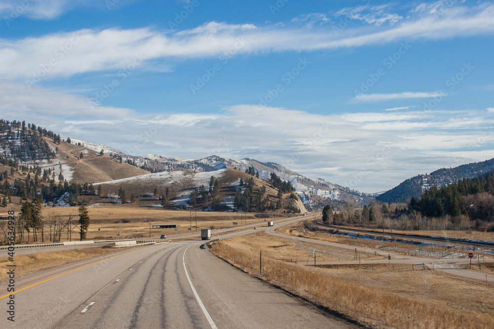 Beautiful autumn landscape on a bright sunny day, which depicts a highway, high mountains ahead and a clear blue sky with fluffy gray-white clouds