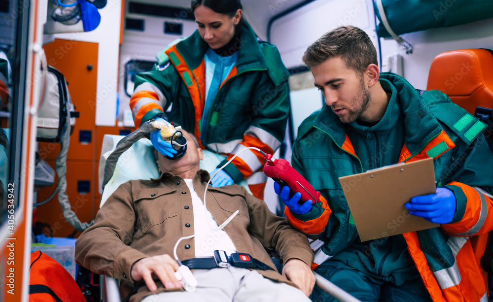 Paramedics are working with a senior man patient while he lies on a stretcher in an ambulance. Paramedics are working with a senior man patient while he lies on a stretcher in an ambulance.