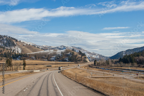 Beautiful autumn landscape on a bright sunny day, which depicts a highway, high mountains ahead and a clear blue sky with fluffy gray-white clouds