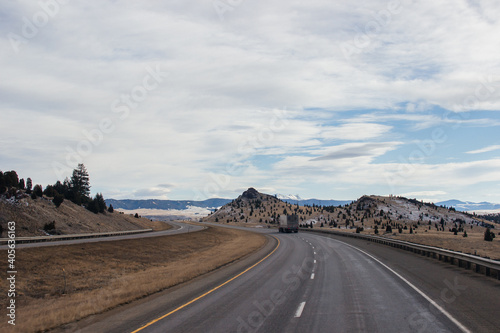 Beautiful autumn landscape on a bright sunny day, which depicts a highway, high mountains ahead and a clear blue sky with fluffy gray-white clouds