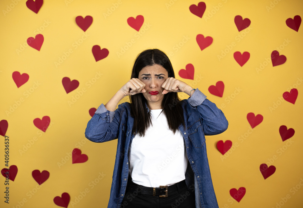 Young caucasian woman over yellow background with red hearts depressed and worry for distress, crying angry and afraid. Sad expression. Young caucasian woman over yellow background with red hearts depressed and worry for distress, crying angry and afraid. Sad expression.