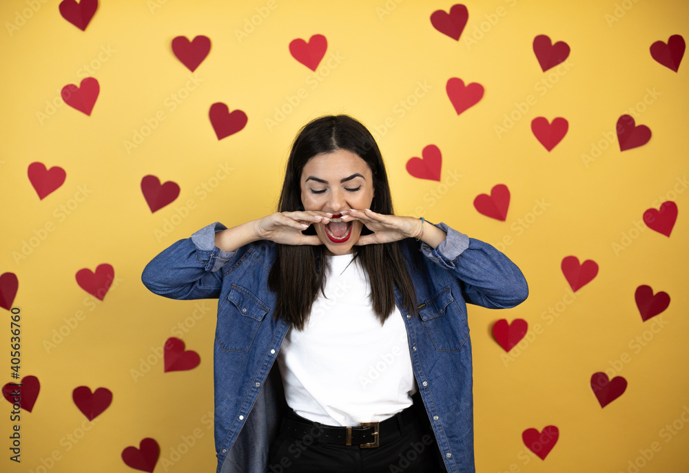 Young caucasian woman over yellow background with red hearts shouting and screaming loud down with hands on mouth Young caucasian woman over yellow background with red hearts shouting and screaming loud down with hands on mouth