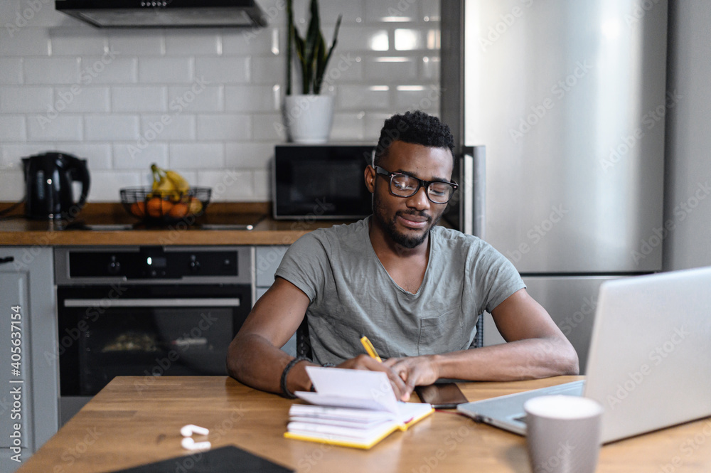 African american male freelancer sitting at the desk, look at the laptop screen. Happy young student taking notes, remotely studying. Successful business man searching ideas, working on project African american male freelancer sitting at the desk, look at the laptop screen. Happy young student taking notes, remotely studying. Successful business man searching ideas, working on project