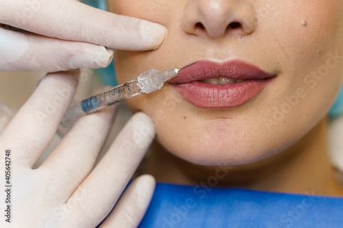 Close-up lips augmentation injections for attractive girl. Plastic surgeon does injection in lip in medical clinic. Cosmetic rejuvenating facial treatment. Empty space for advert