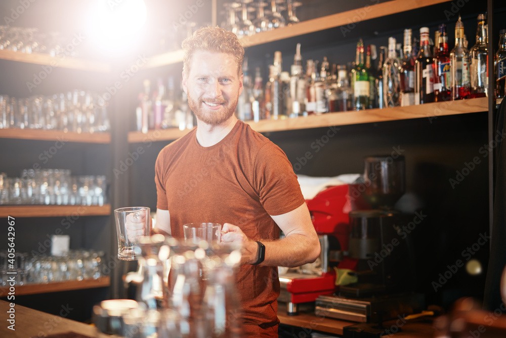 A bartender standing in a bar and wiping glass.