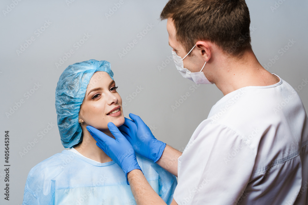 Consultation with plastic surgeon on white background. Cosmetic rejuvenating facial treatment. Doctor man with blue medical gloves touches girl face. Patient ask about lips and chin injections