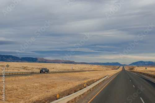 Asphalt road among steppes with yellow dry grass, blue mountains on the horizon, beautiful blue-gray autumn sky. Montana, USA, 11-23-2019