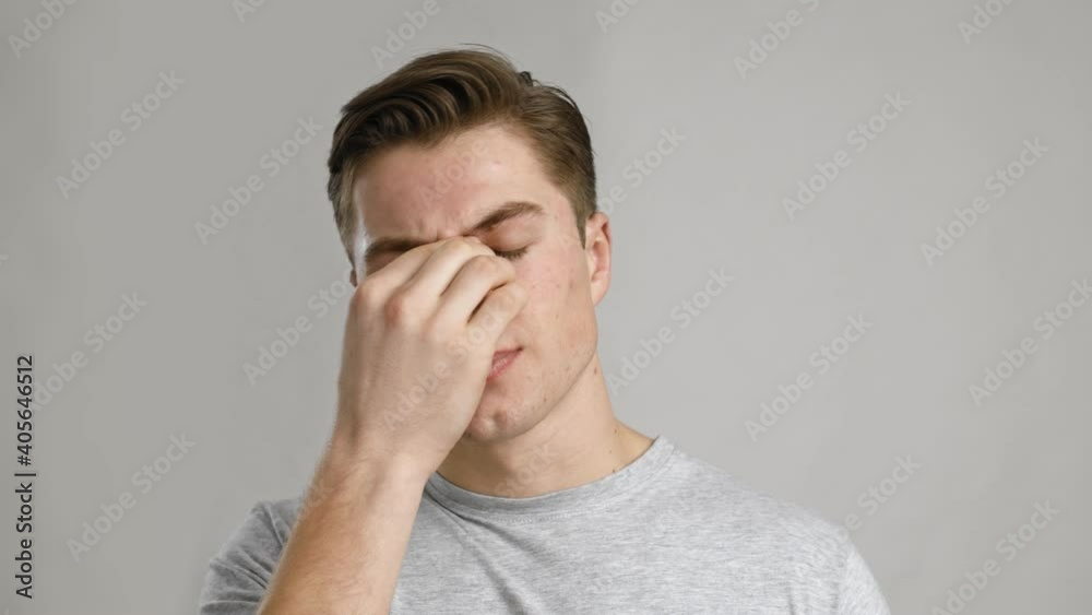 Close up portrait of young sick man rubbing his sore nose, grey studio background, slow motion Close up portrait of young sick man rubbing his sore nose, grey studio background, slow motion