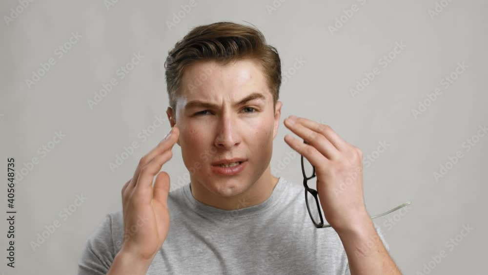 Young tired man taking off his glasses and rubbing his eyes, grey studio background, slow motion Young tired man taking off his glasses and rubbing his eyes, grey studio background, slow motion