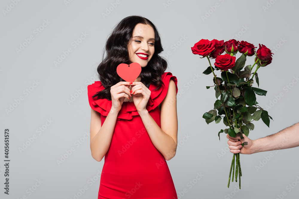 man giving roses to happy woman in red dress holding heart-shaped card isolated on grey man giving roses to happy woman in red dress holding heart-shaped card isolated on grey