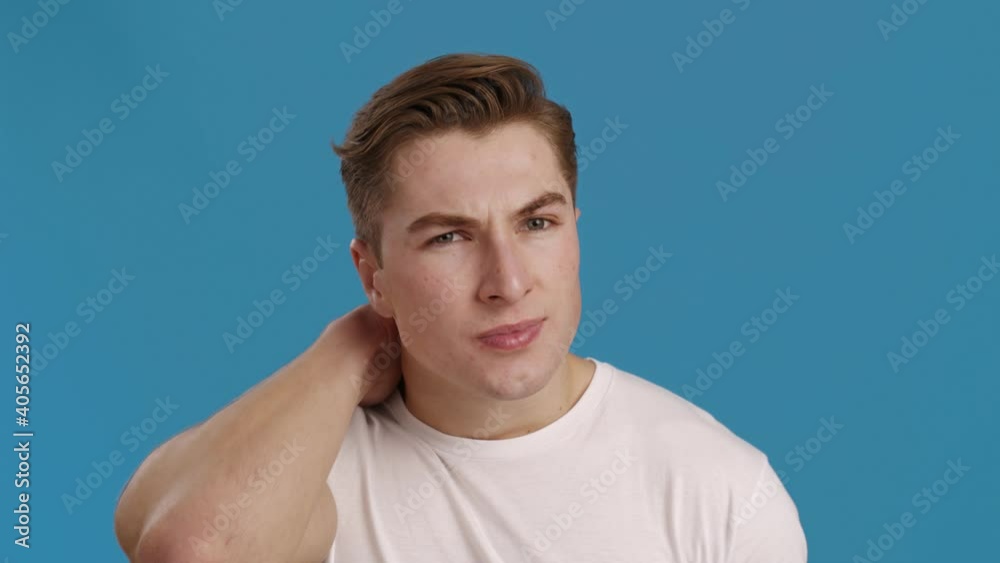 Young man massaging his painful neck, blue background, slow motion