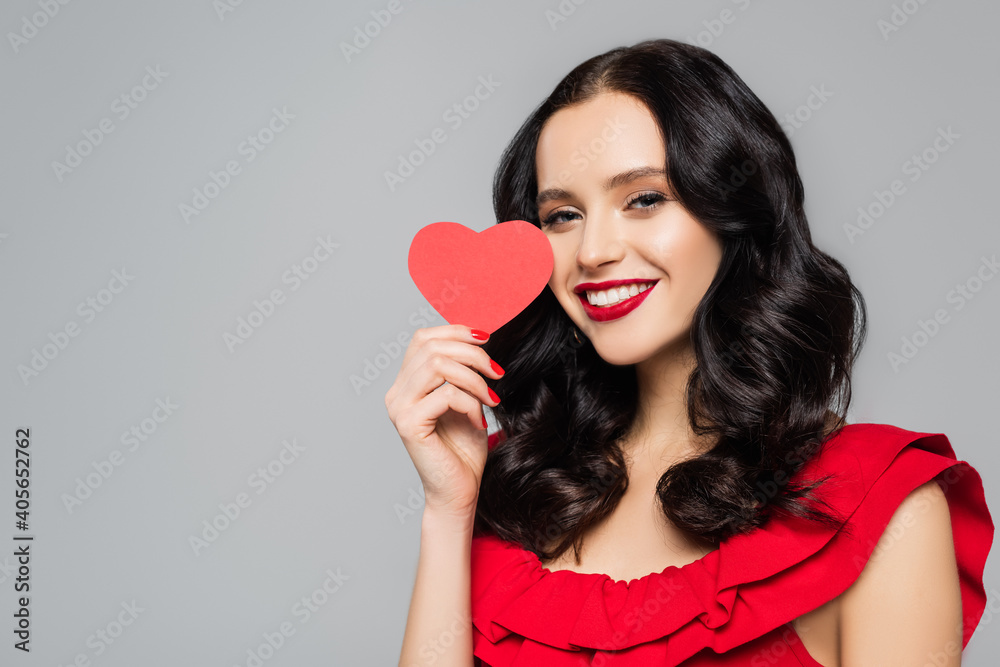 smiling young woman holding red paper heart isolated on grey smiling young woman holding red paper heart isolated on grey