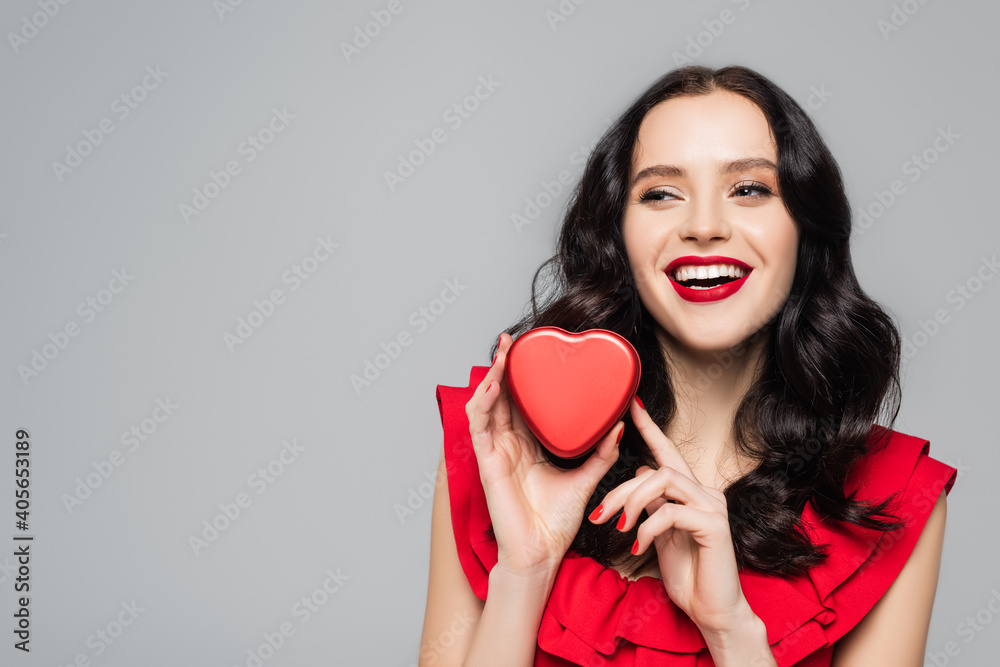 cheerful woman with red lips holding heart-shaped gift box isolated on grey cheerful woman with red lips holding heart-shaped gift box isolated on grey