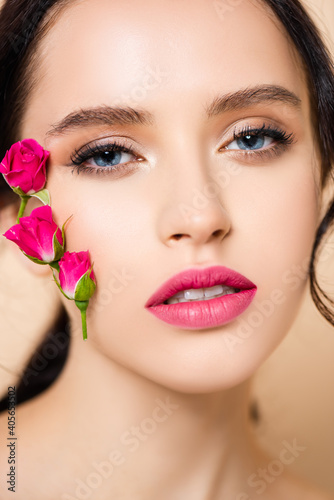 close up of sensual young woman with flowers on face looking at camera isolated on pink