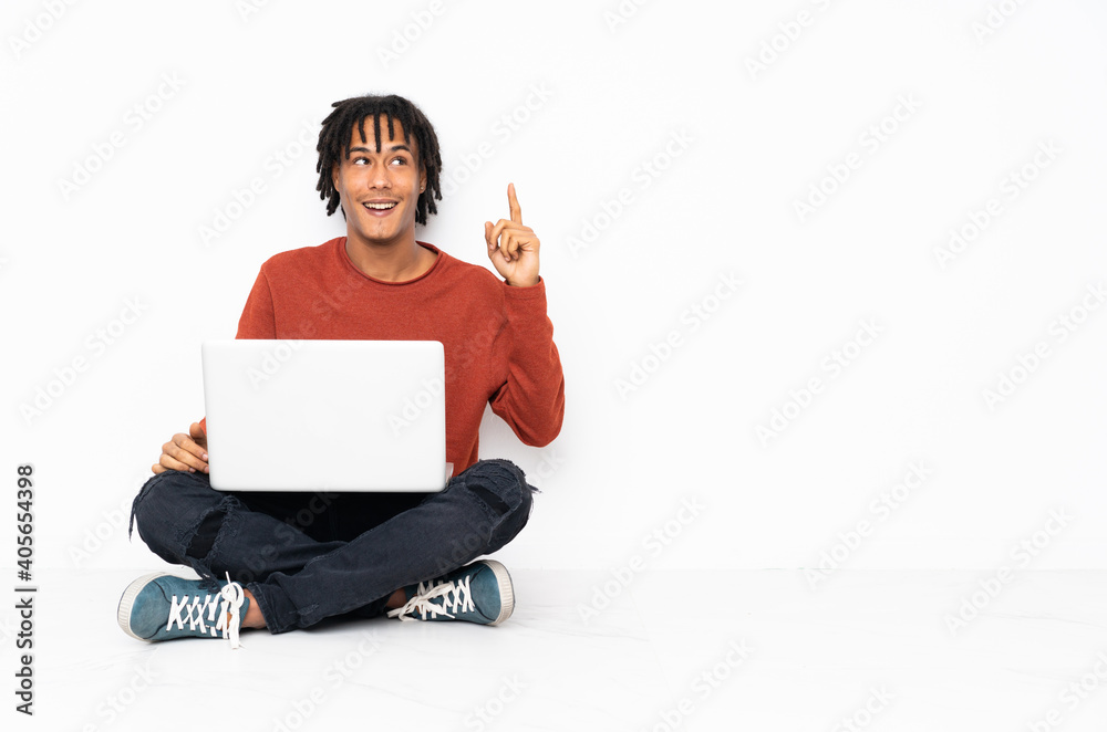 Young african american man sitting on the floor and working with his laptop intending to realizes the solution while lifting a finger up Young african american man sitting on the floor and working with his laptop intending to realizes the solution while lifting a finger up