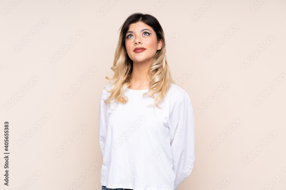 Teenager girl isolated on beige background and looking up Teenager girl isolated on beige background and looking up