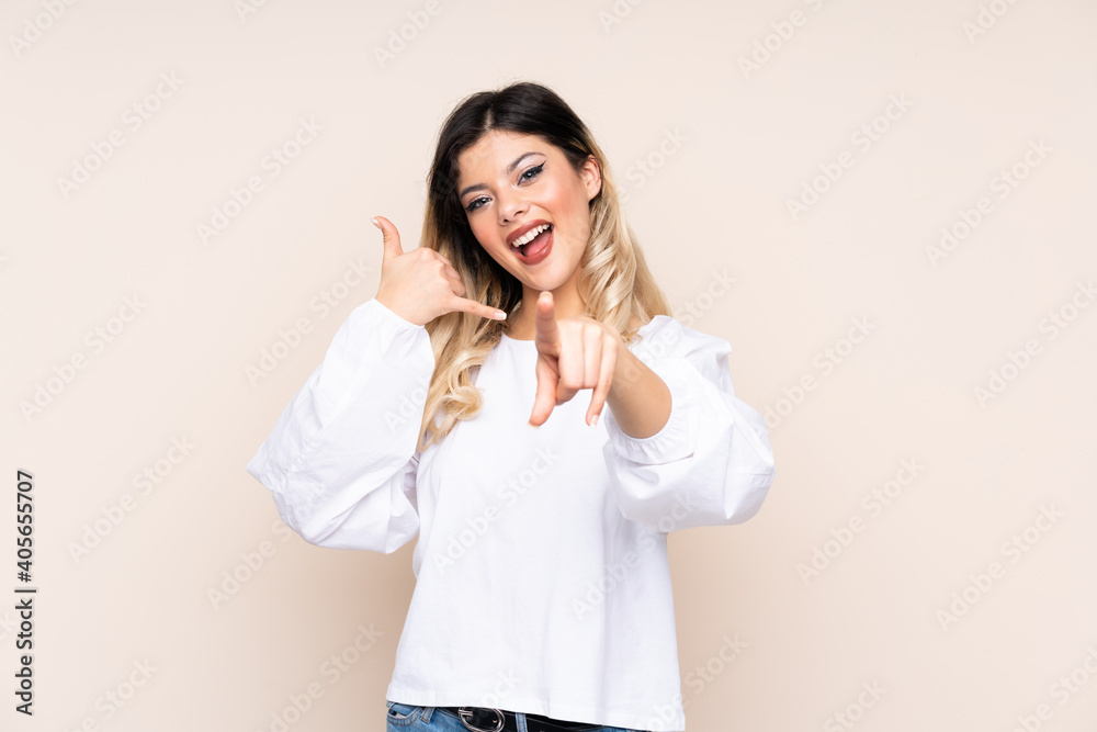 Teenager girl isolated on beige background making phone gesture and pointing front